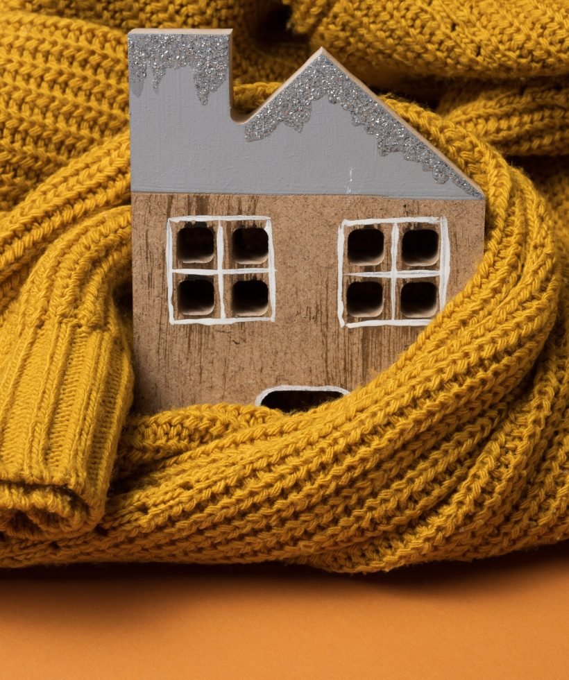 the wooden model of the house is wrapped in a warm knitted sweater. Loan concept for house insulation, alternative energy